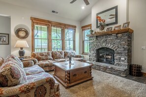Ein Wohnzimmer mit Kamin aus Stein, gemusterten Sofas, einem Couchtisch und großen Fenstern.