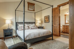 Ein Bett mit Baldachin, ein Holzkopfende, zwei Nachttische, ein gemustertes Teppich und eine Holztür zum Badezimmer.