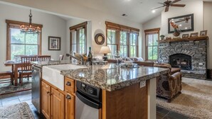 A spacious kitchen with granite countertops, wooden cabinets, a dishwasher, and a stone fireplace. - Lodges 1140 | Shuttle | Shared Hot Tub (Mammoth Lakes)