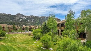 A resort with multiple wooden buildings, a grassy lawn, and a mountain backdrop. - Lodges 1140 | Shuttle | Shared Hot Tub (Mammoth Lakes)
