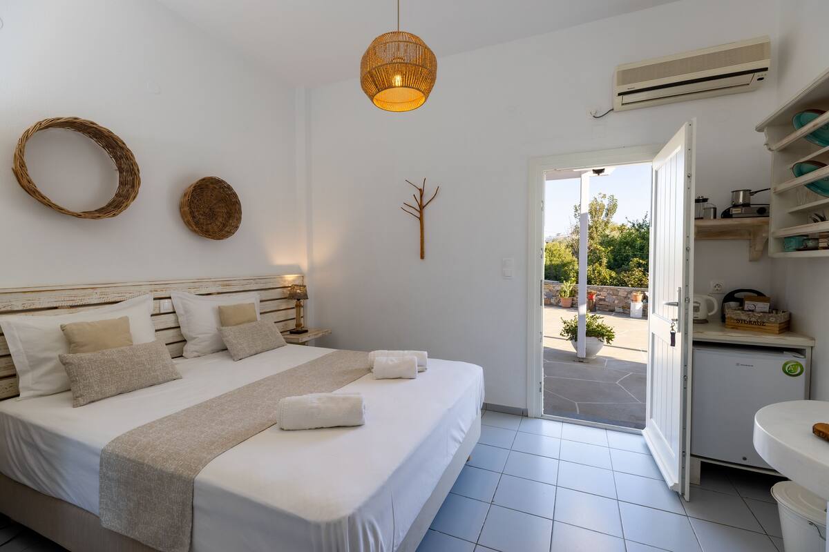 A modern bedroom with a large bed, a bedside table, a hanging light fixture, and a view of the outdoors.