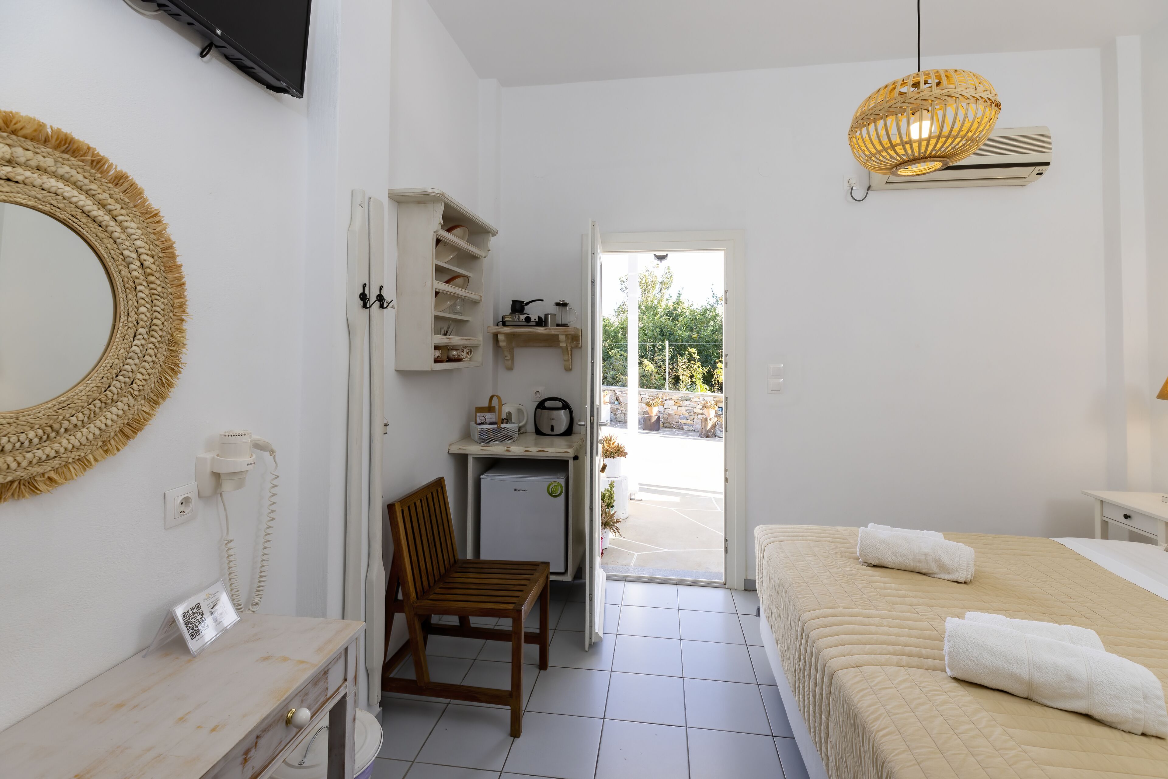 A hotel room with a bed, a desk, a chair, a small kitchenette, and a view of the outdoors.