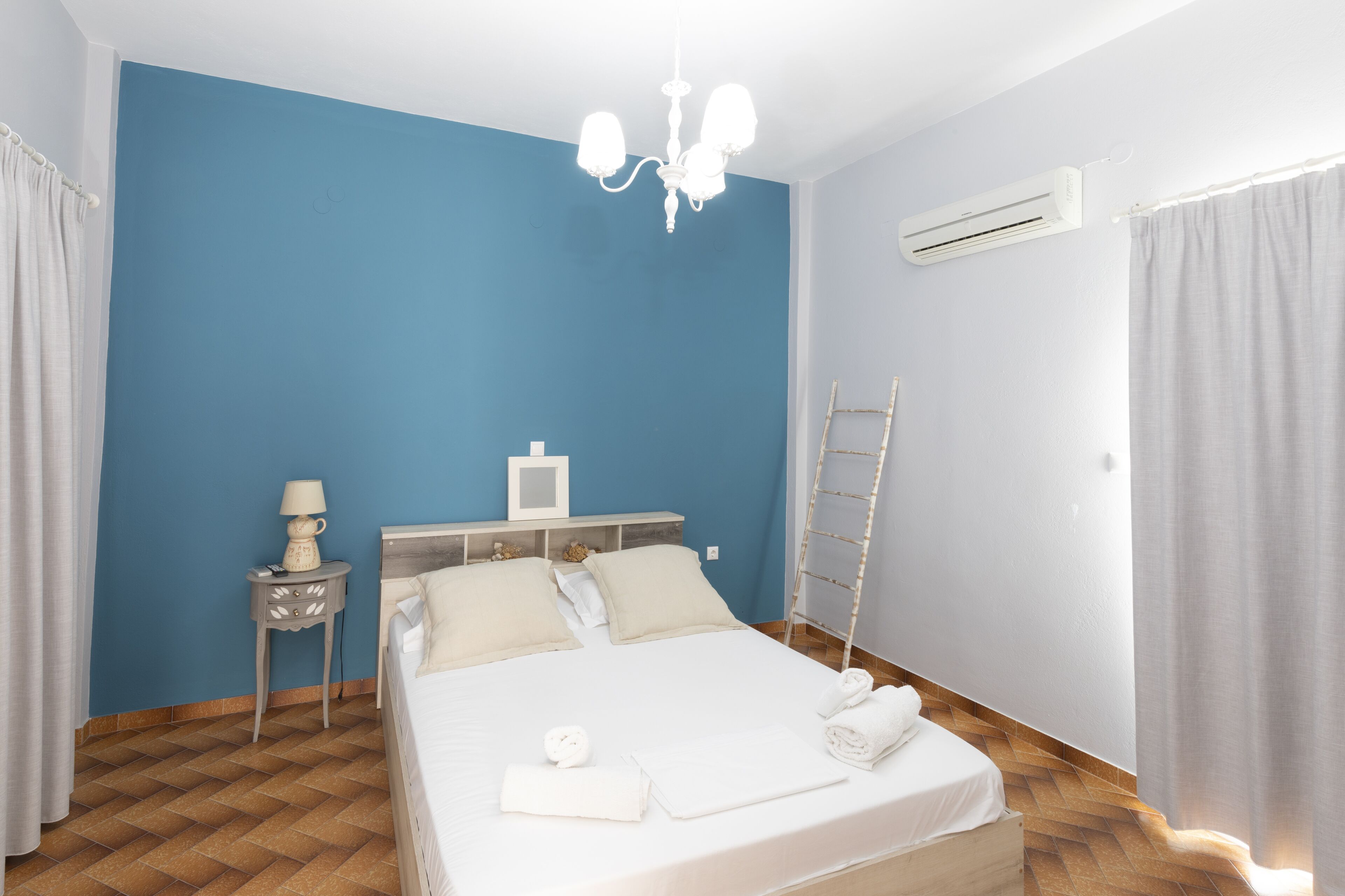 A bedroom with a bed, a nightstand, a lamp, a ladder, and an air conditioning unit.