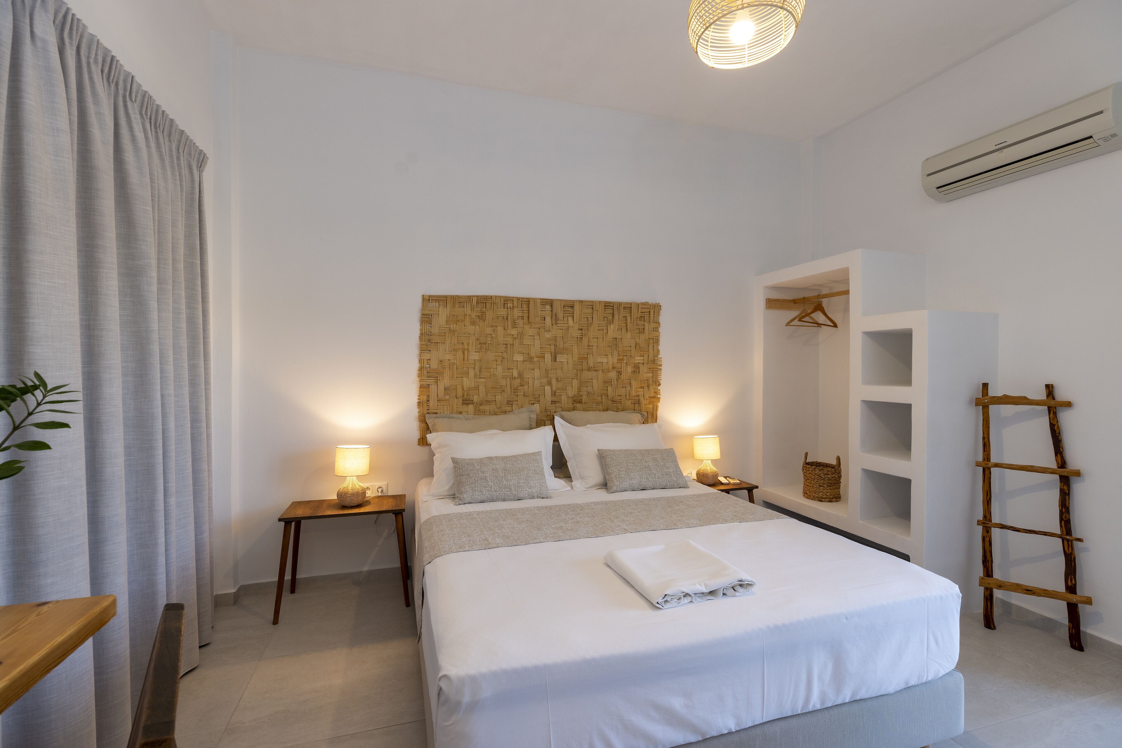 Een netjes ingerichte slaapkamer met een groot bed, nachtkastjes met lampen, een hangmand en een houten ladder.