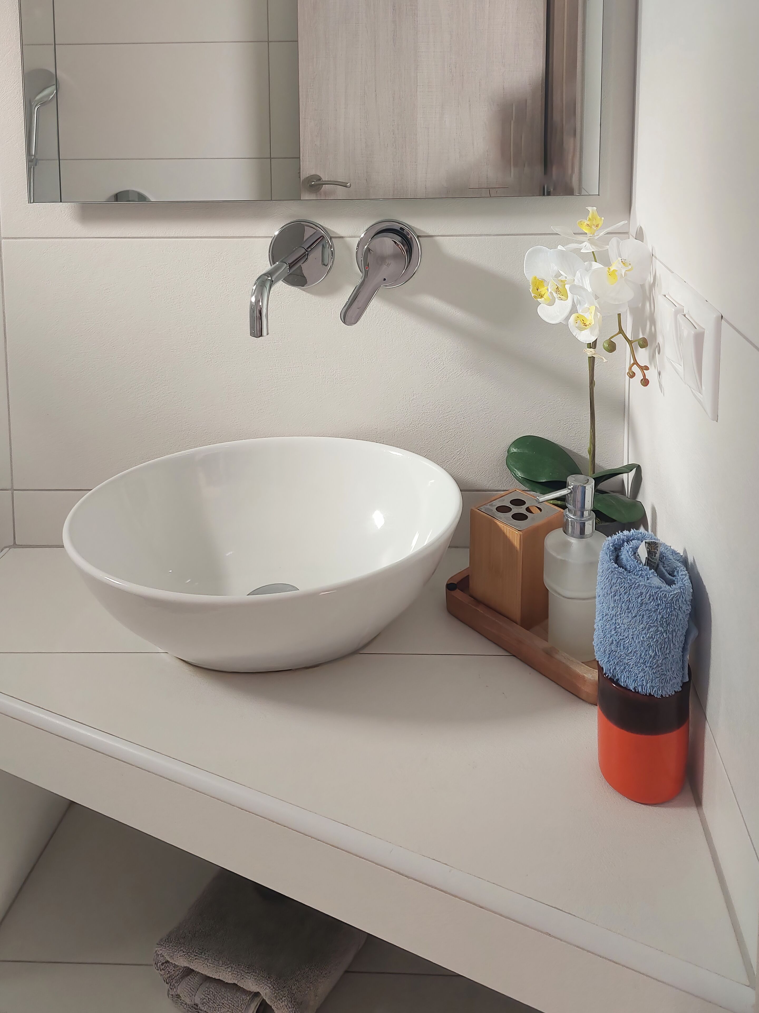 A bathroom with a white sink, a mirror, a towel, a blue towel, and a potted orchid.