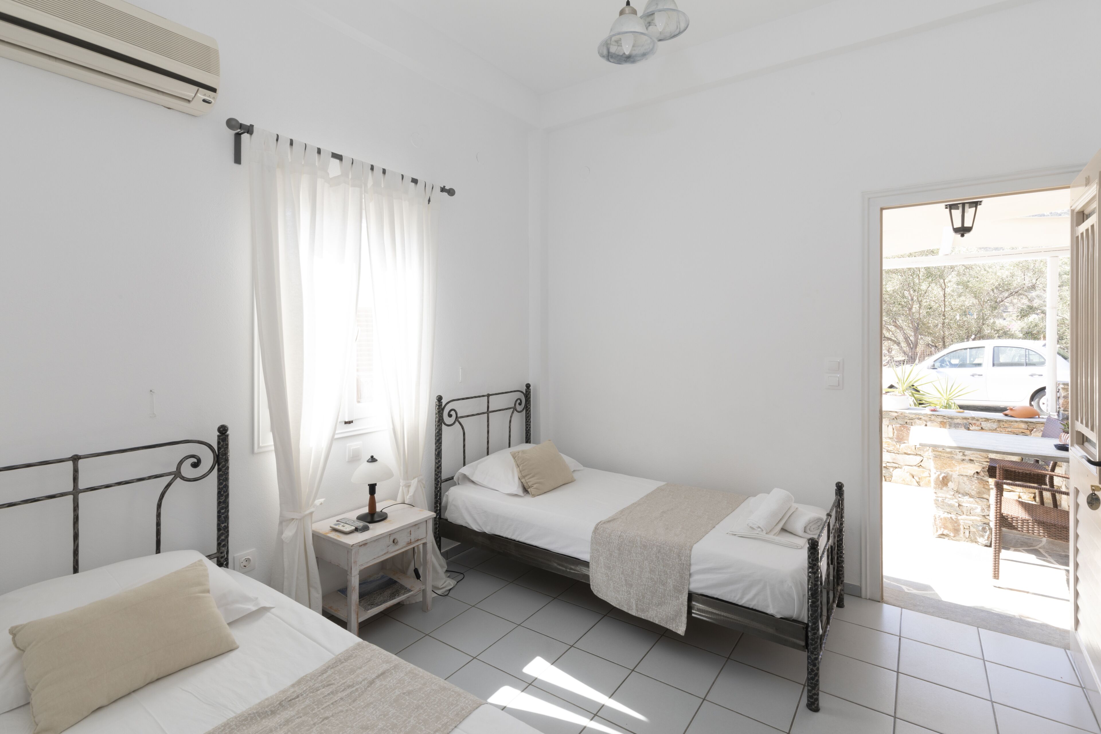 A bedroom with two beds, a desk with a lamp, and a view of the outside.