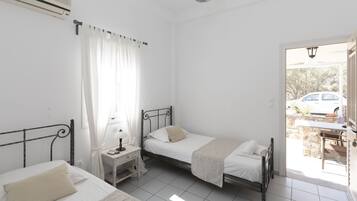 A bedroom with two beds, a desk with a lamp, and a view of the outside.