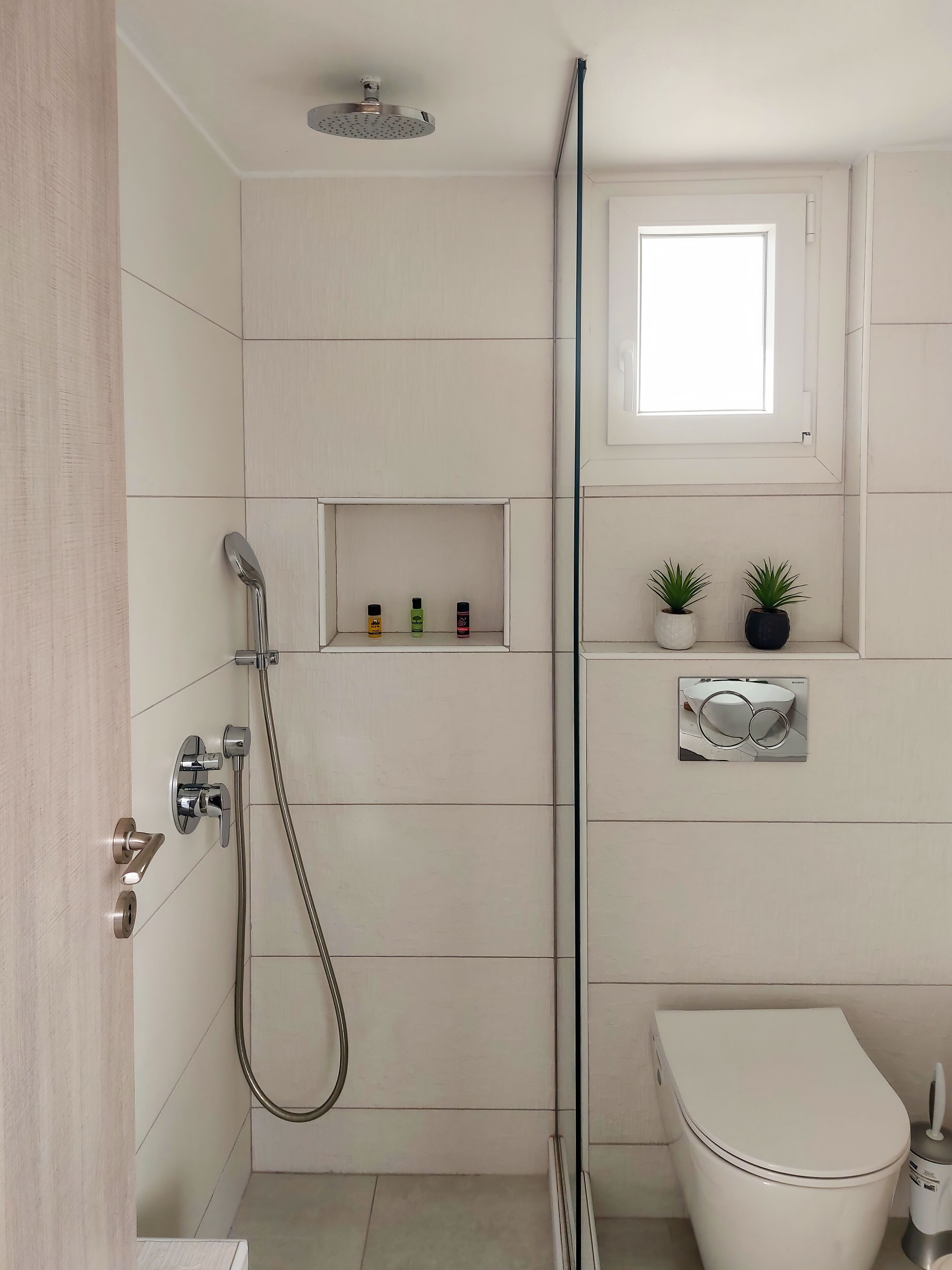 Moderni kylpyhuone, jossa on suihku, wc ja pieni ikkuna pesualtaan yläpuolella.