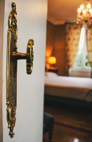 Un picaporte de bronce con diseños intrincados, que da acceso a una habitación con una cama y una mesita de noche con una lámpara.