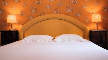 Un lit avec une tête de lit incurvée, deux lampes de chevet et un papier peint à motifs.