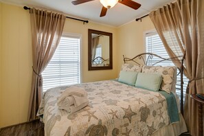 Un dormitorio con cama, cortinas, ventilador de techo y ventana con persianas.
