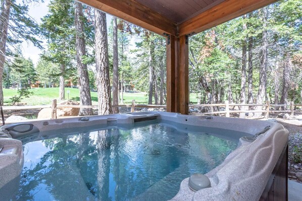 Relax in a serene hot tub surrounded by a natural forest setting and shaded wooden deck.