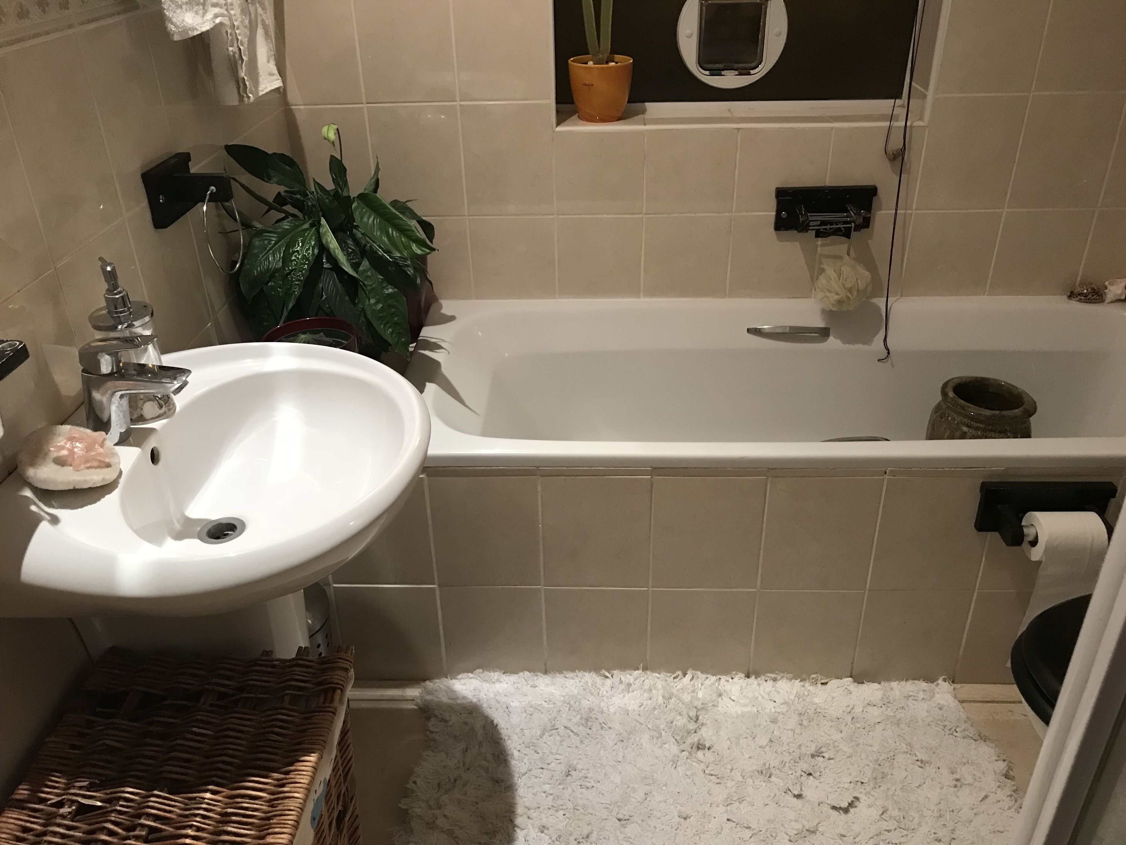 A bathroom with a white sink, a bathtub, and a white fluffy rug.