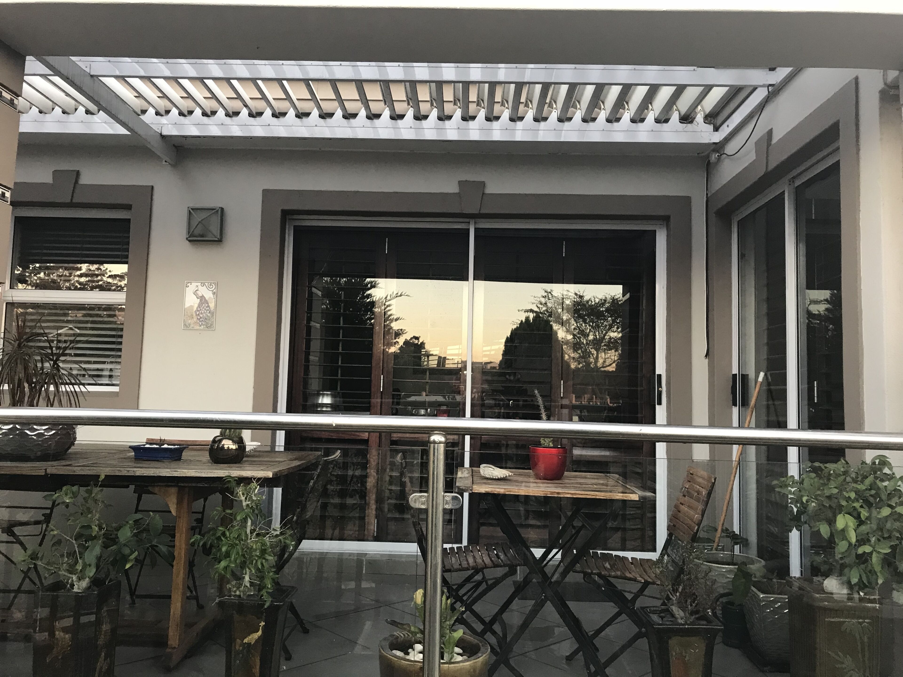 An outdoor patio area with a table and chairs, potted plants, and a pergola structure.