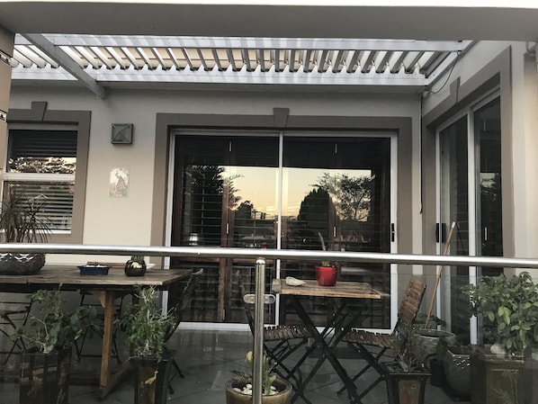 An outdoor patio area with a table and chairs, potted plants, and a pergola structure.