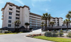 Un hôtel à plusieurs étages doté de balcons, de palmiers et d’un espace de stationnement.