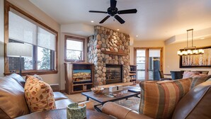 A spacious living room with a stone fireplace, leather sofas, a coffee table, and a television. - CX313 | Ski In/Out | Spacious Floorplan | Winter Shuttle | Great Amenities (Steamboat Springs)