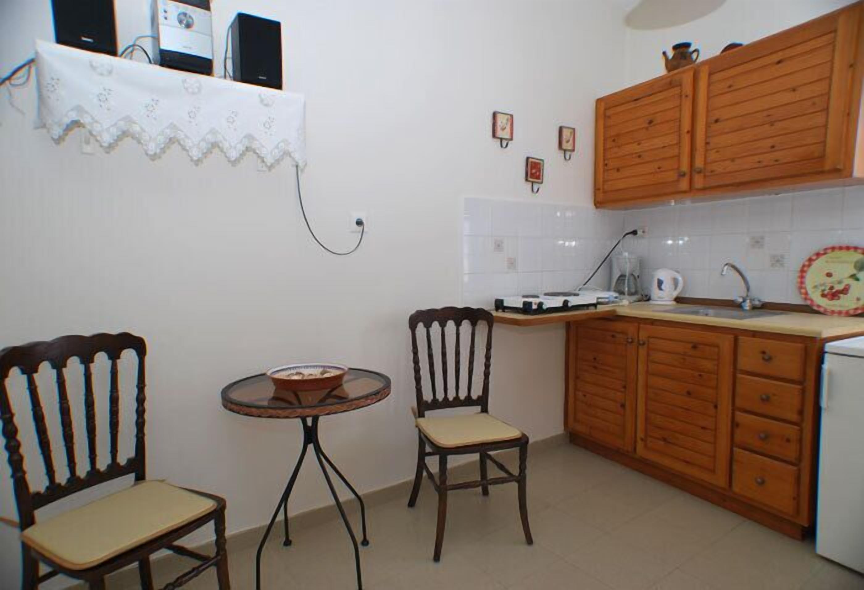 Una cocina pequeña con armarios de madera, una mesa redonda, dos sillas y algunos electrodomésticos.