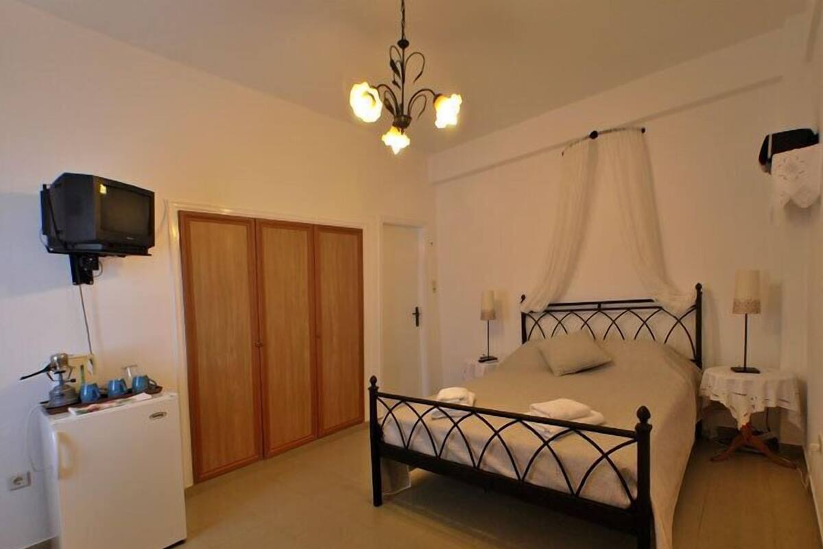 Un dormitorio con cama, armario, televisor y mesita de noche con lámpara.