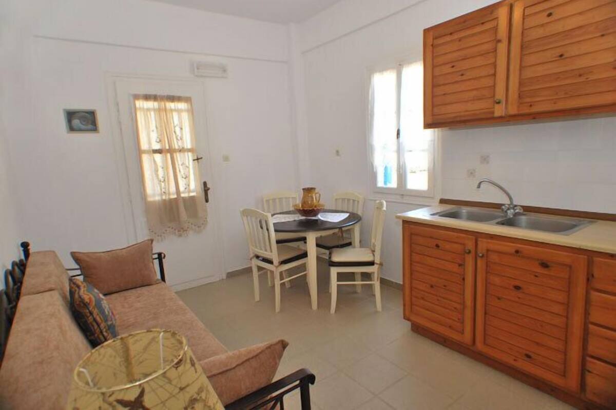 Un espacio habitable compacto con sofá, mesa de comedor, sillas y una cocina con armarios de madera y un fregadero.