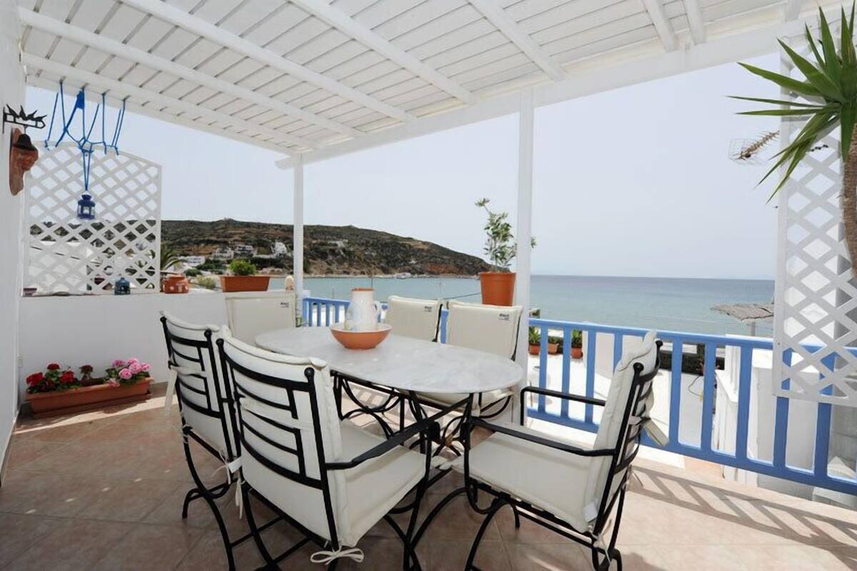 Un espacio de estar al aire libre cubierto, con una mesa y sillas, que ofrece vistas a la costa.