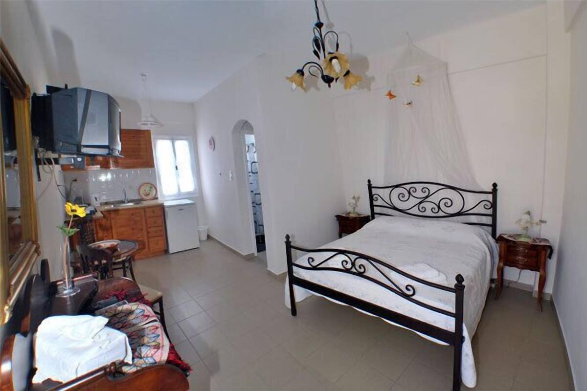 Un dormitorio con cama, mesitas de noche, televisor y una zona de cocina al fondo.