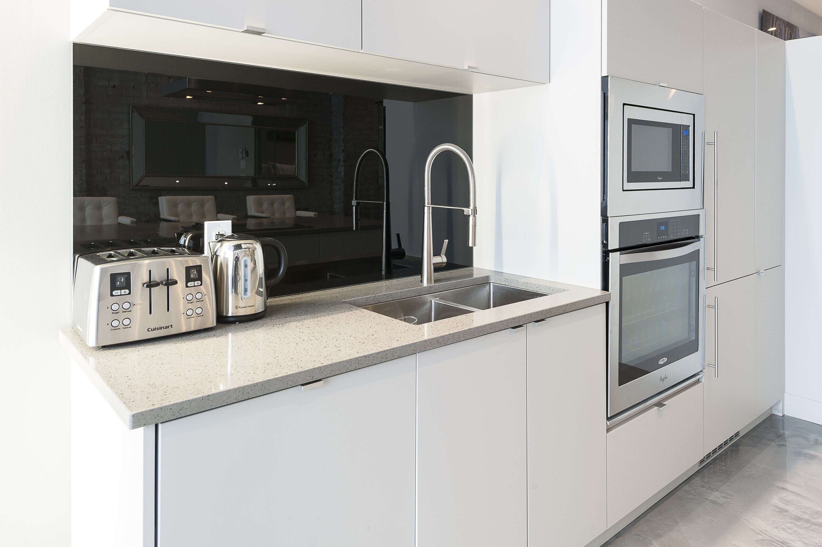 Een moderne keuken met witte kasten, een roestvrijstalen afzuigkap, een dubbele oven en een inbouwgootsteen.