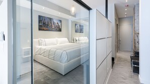 Une chambre moderne avec un grand lit, une cloison en verre et un tableau représentant un paysage urbain accroché au mur.