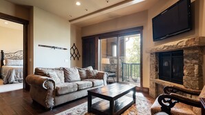 A spacious living room with a stone fireplace, a large flat-screen TV mounted above it, and a comfortable seating area with a sofa and armchairs. - Canyons Townhome, Views & Gondola Access (Park City)