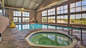 An indoor swimming pool with a hot tub, stone flooring, and large windows offering a view of the outdoors.