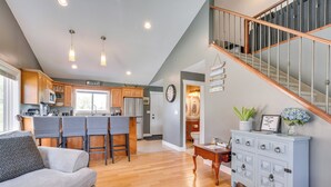 A spacious living area with a sofa, a coffee table, and a blue cabinet. There is a kitchen in the background with wooden cabinets and a bar area.