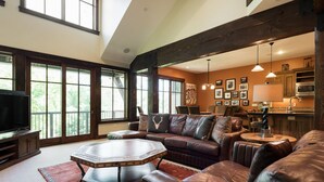A spacious living room with a large sectional sofa, a coffee table, and a television. There are large windows providing natural light and a view of the outdoors. - Silver Star 15 | Steps to Lift | Hot Tub (Park City)
