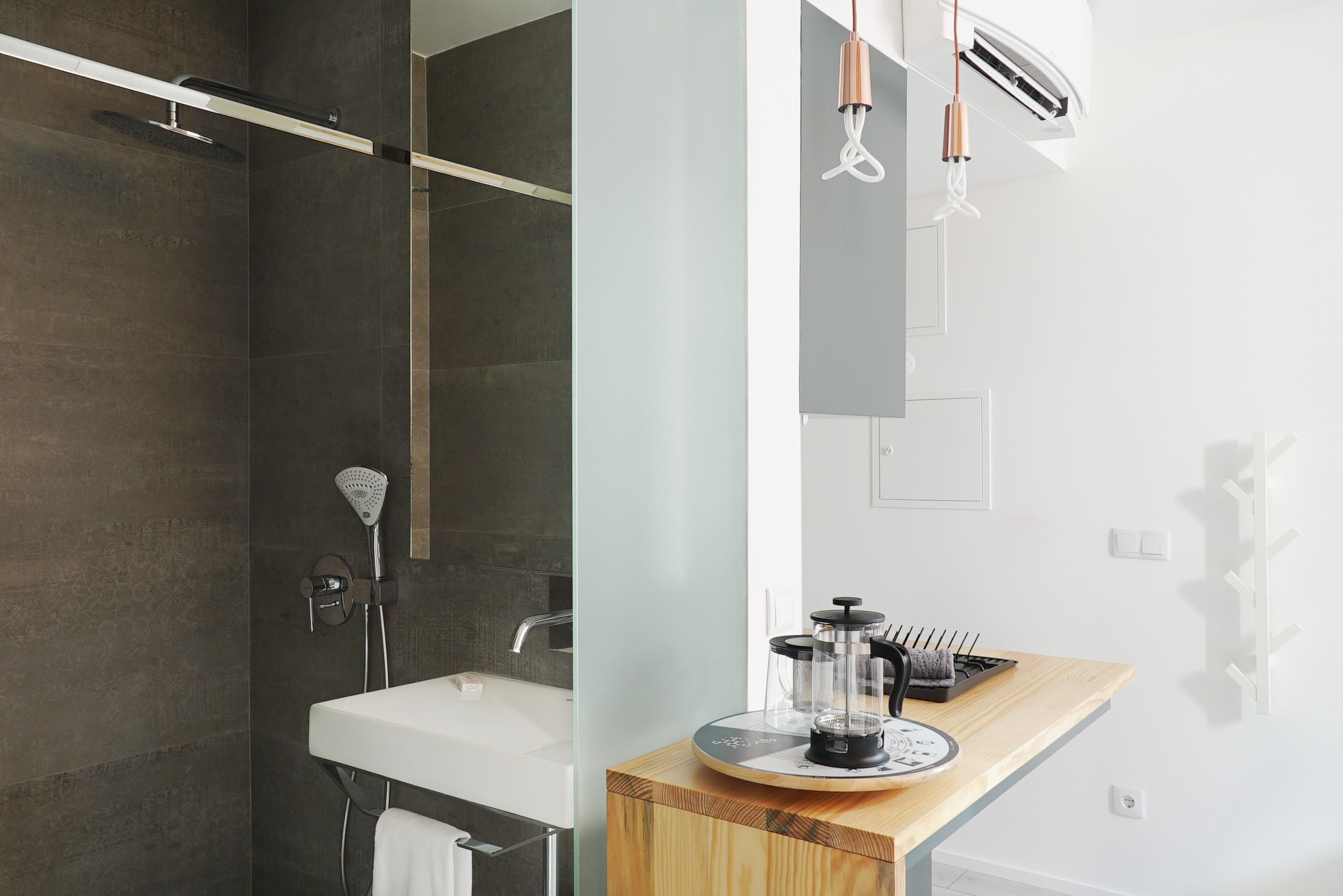 A modern bathroom with a shower, a sink, and a coffee maker on a wooden countertop.