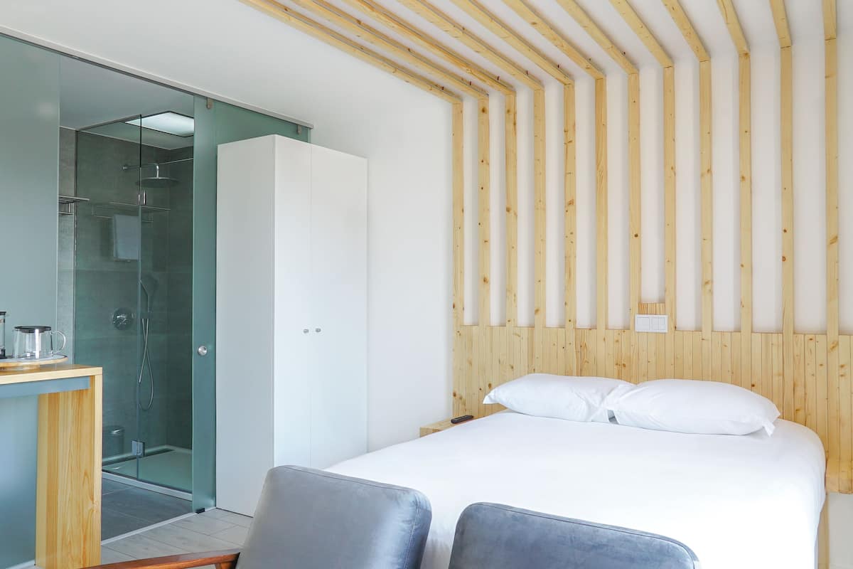 A modern bedroom with a wooden headboard, a glass shower enclosure, and a bedside table with a lamp.