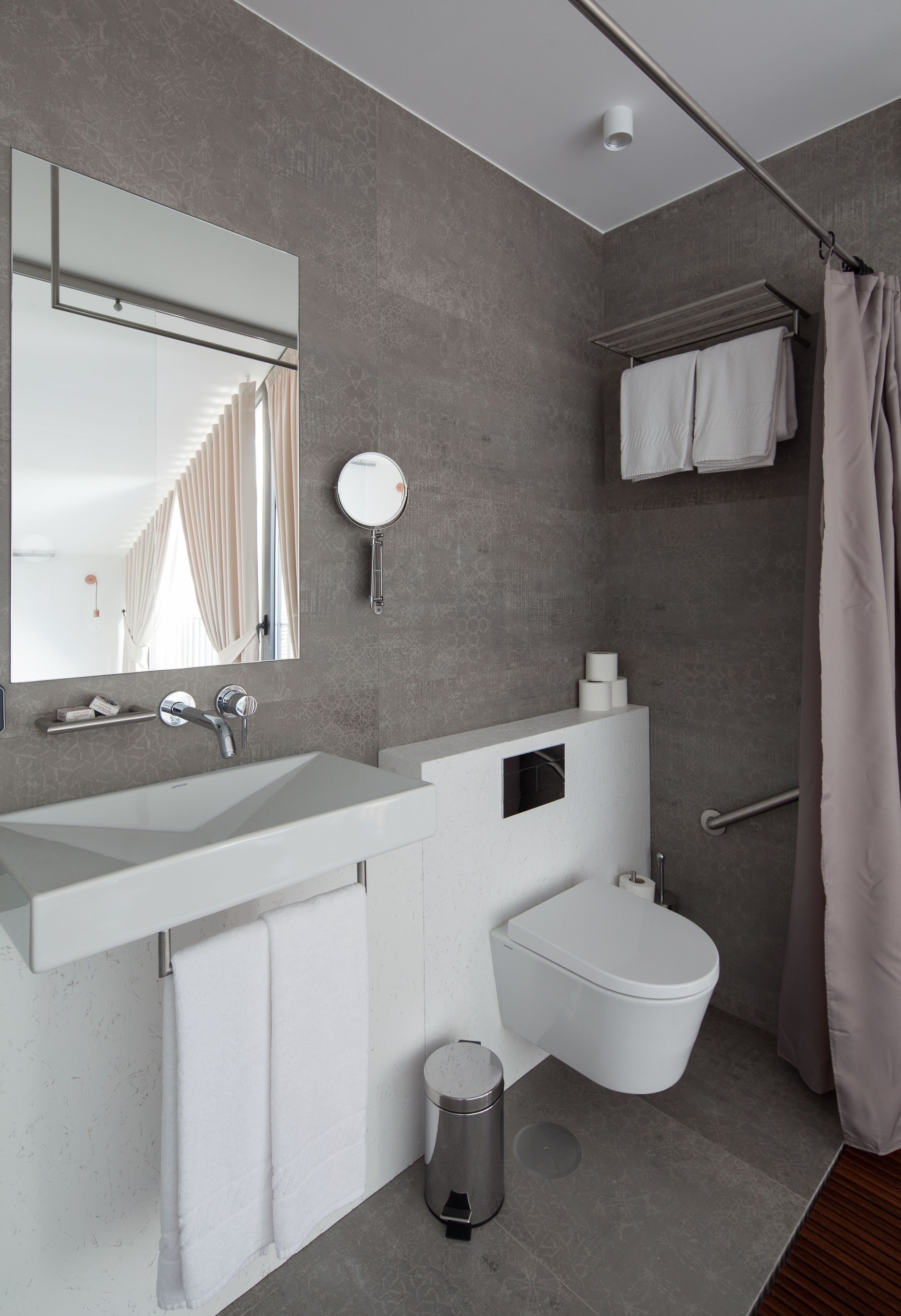 Un baño moderno con un espejo grande, lavabo blanco y retrete.