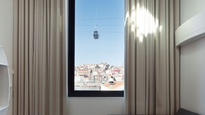 A modern living room with a large window, a sofa, and a view of a cityscape and cable car. - 7g Roaster Apartments (Vila Nova de Gaia)