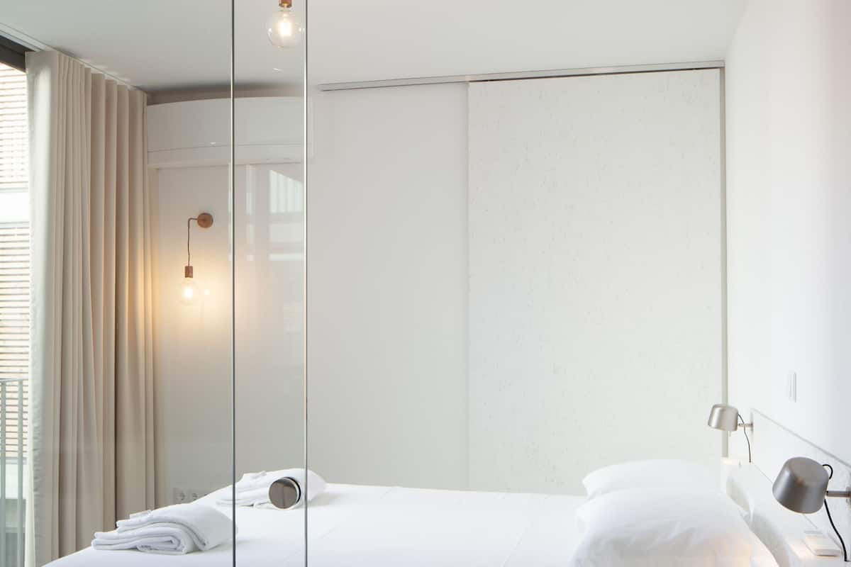 A modern bedroom with a large bed, a glass partition, and a bedside table with a lamp.