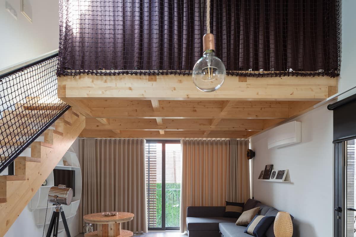 A modern loft-style living space with a wooden staircase, a round wooden table, and a sofa with cushions.