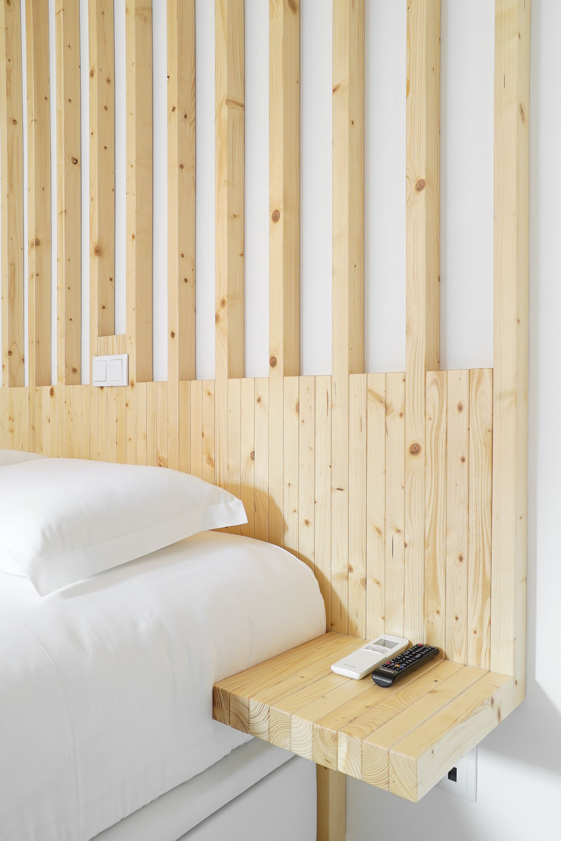 A bed with white linens, a wooden headboard, and a bedside table with a remote control.