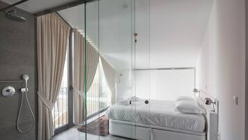 Une chambre moderne avec une cloison en verre, une douche, un lit et une vue sur l’extérieur.
