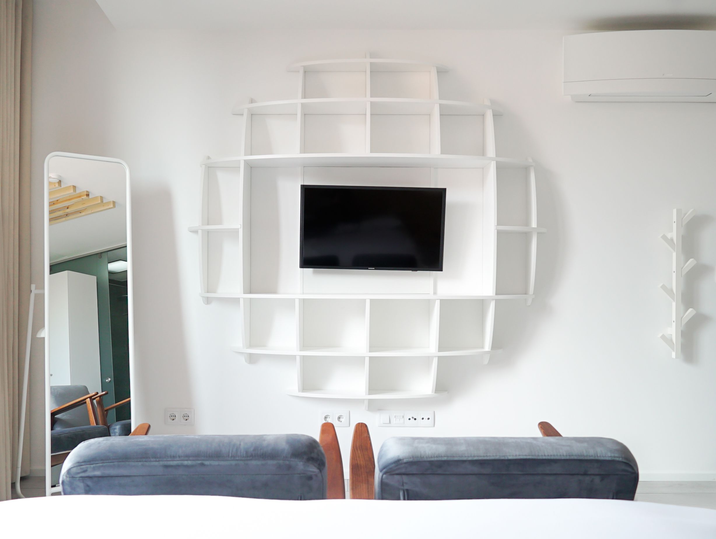 Une chambre d’hôtel moderne dotée d’un téléviseur central, d’étagères intégrées et d’un coin salon avec deux poufs.