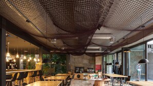 A modern restaurant with wooden tables and chairs, a stone wall, and hanging lights. - 7g Roaster Apartments (Vila Nova de Gaia)