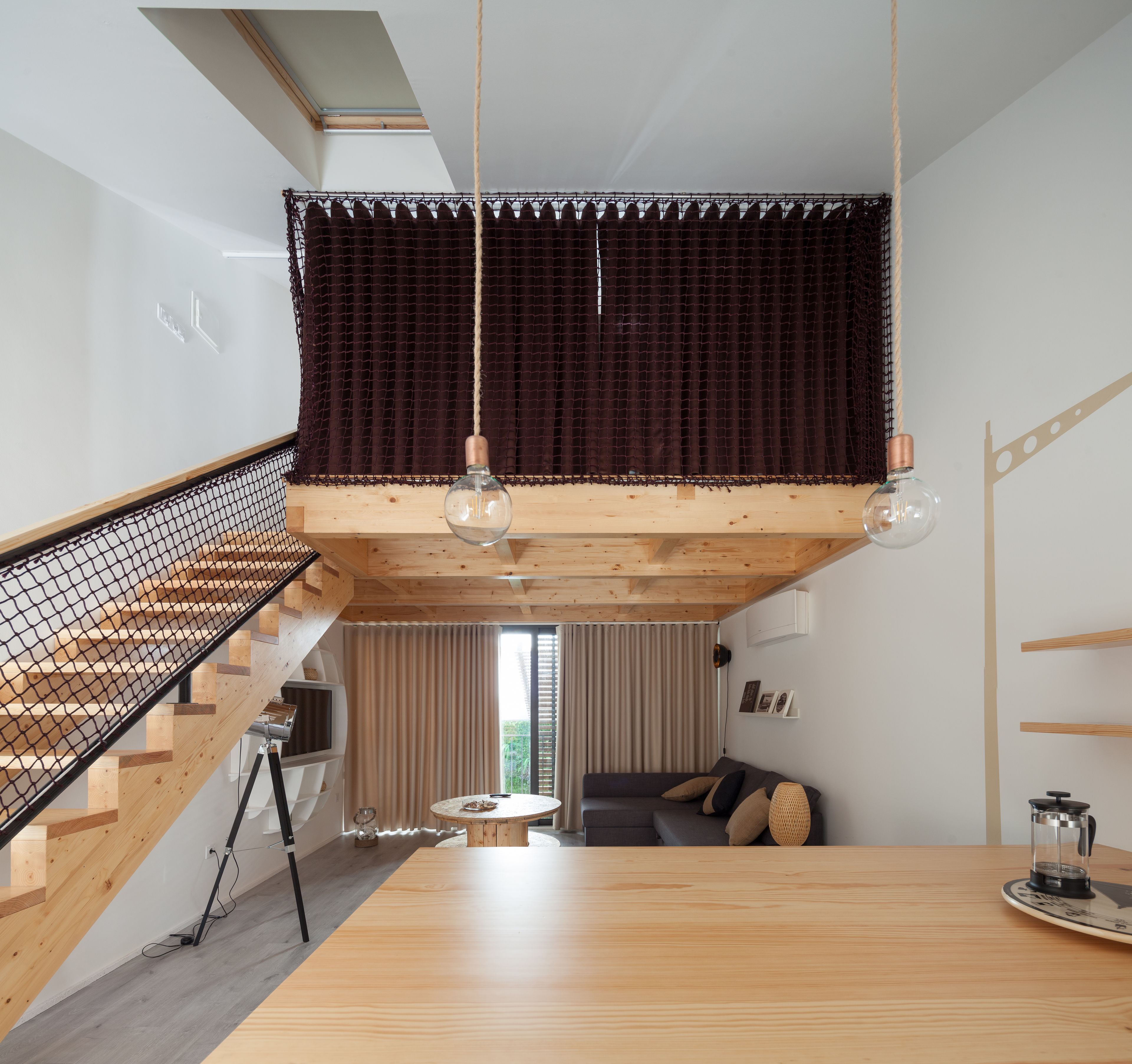Un espai modern estil loft amb una escala de fusta, un nivell entreplà i una zona de menjador.