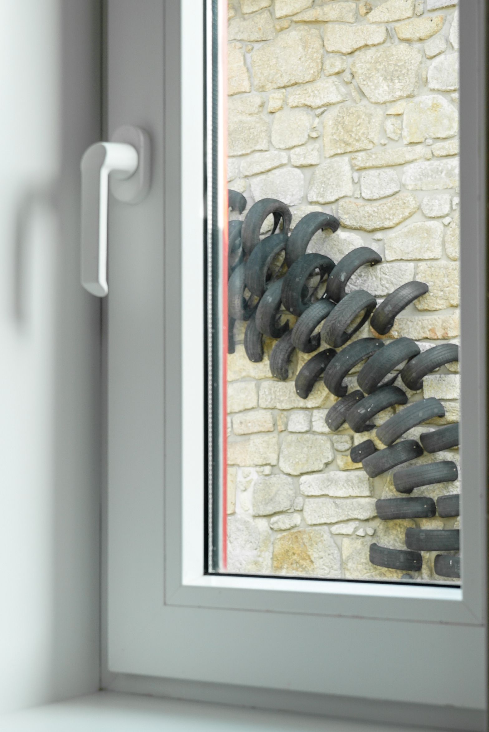 Une porte avec une poignée blanche et une fenêtre avec un mur en pierre et des joints en caoutchouc noir.