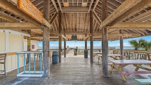 Une terrasse extérieure en bois, dotée de tables de pique-nique et de poubelles, avec vue sur une plage.