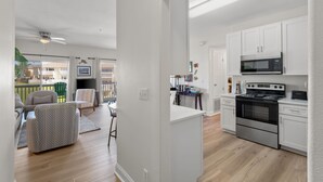 Une cuisine moderne avec des meubles blancs, une cuisinière en acier inoxydable et un four à micro-ondes. Un balcon aménagé avec du mobilier d’extérieur offre une vue sur les bâtiments.