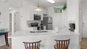 Une cuisine moderne avec des meubles blancs, un îlot central, un four à micro-ondes, une cuisinière, un réfrigérateur et un luminaire suspendu.