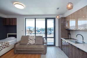 A modern apartment with a kitchenette, a sofa, a bed, and a large window offering a city view. - LUX apartment (Borjomi)