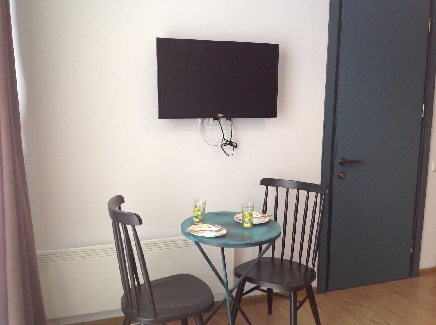 Un pequeño comedor con una mesa redonda y dos sillas, un televisor de pantalla plana en la pared y una puerta cerrada.