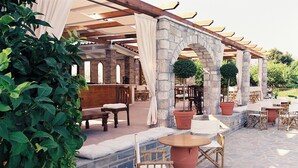 An outdoor patio area with stone flooring, wooden furniture, and a pergola structure. - Nicolas Village Club (Aigialeia)
